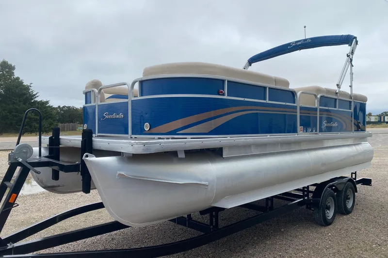 Slide: The Image of 2013 Sweetwater 2286 pontoon boat on trailer, blue and beige design, parked outdoors. - 4