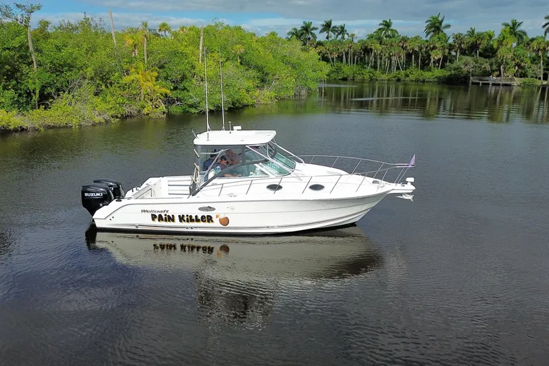 Slide: The Image of 2002 Wellcraft 290 Coastal boat on calm water, surrounded by lush greenery. - 1