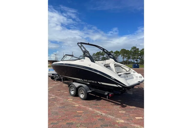 Slide: The Image of 2015 Yamaha Boats 242 Limited S on trailer, parked on brick pavement under blue sky. - 2