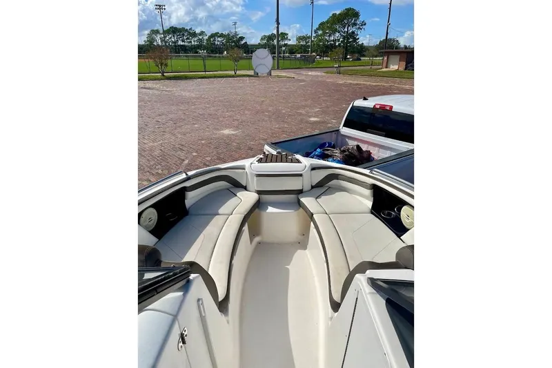 Slide: The Image of 2015 Yamaha Boats 242 Limited S interior with seating, parked near a sports field. - 7