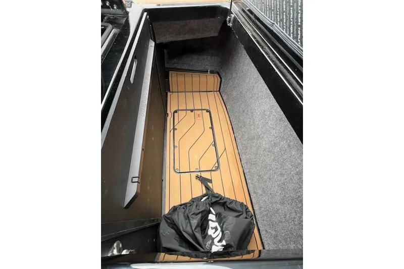 Slide: The Image of 2025 Nautique Super Air Nautique G23 storage compartment with wooden flooring and black bag. - 20