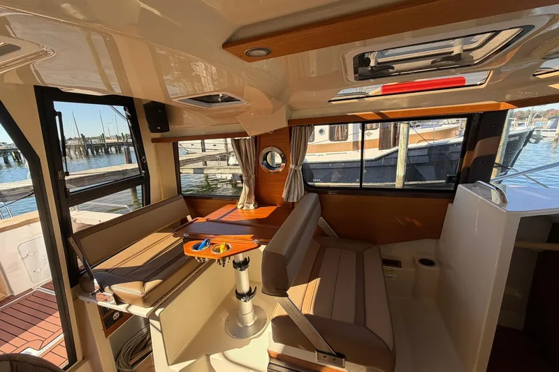 Slide: The Image of 2023 Ranger Tugs R-25 interior with seating, table, and windows overlooking marina. - 32