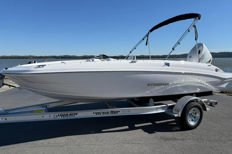 The Image of 2026 Stingray 182 SC boat on trailer by a lake, under clear blue sky. - 1