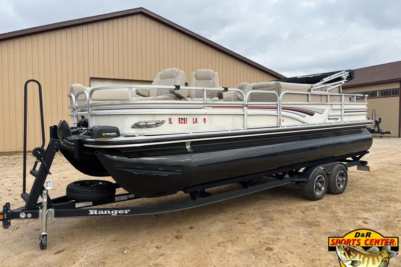 Slide: The Image of 2021 Ranger 223FC pontoon boat on trailer, parked near a beige building. - 0