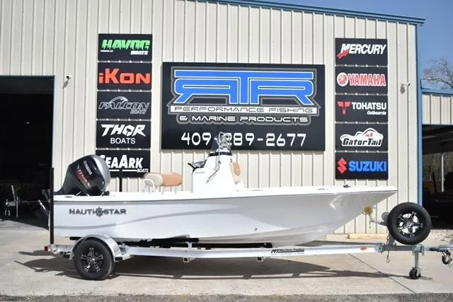 The Image of 2025 NauticStar 194 Bay boat on trailer outside marine shop with various brand signs. - 1