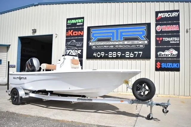 Slide: The Image of 2025 NauticStar 194 Bay boat on trailer outside marine products store. - 2