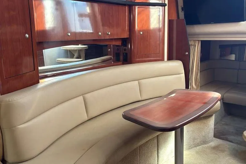 Slide: The Image of 2006 Sea Ray 340 Sundancer interior with beige seating, wooden cabinets, and a small table. - 9