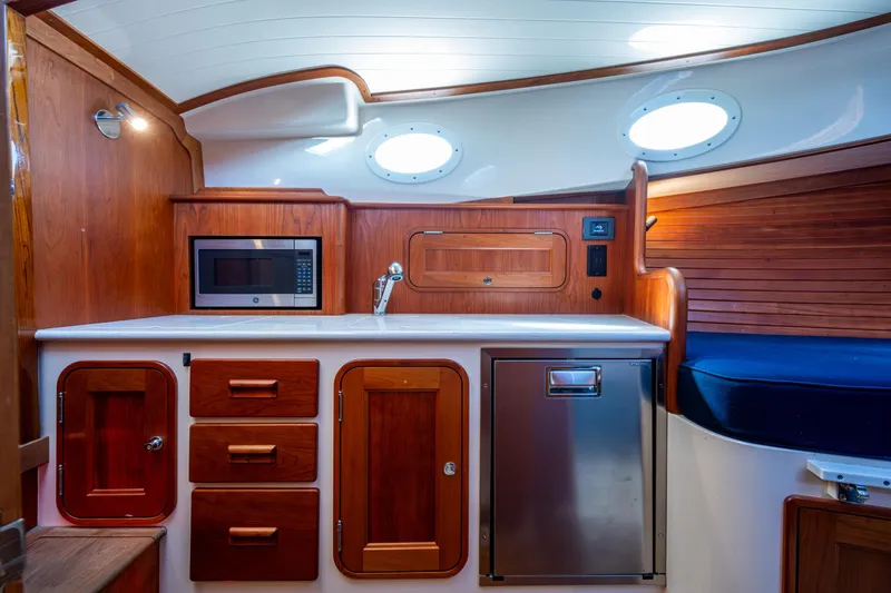 Slide: The Image of 2024 Hinckley 35 yacht interior with wooden cabinetry, microwave, and stainless steel fridge. - 45