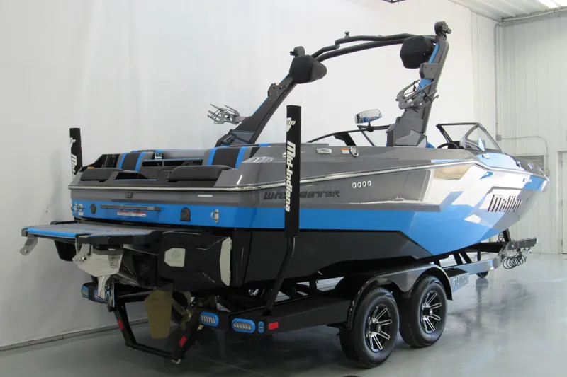 Slide: The Image of 2026 Malibu Wakesetter 22 MXZ boat in showroom, featuring sleek design and vibrant blue accents. - 2