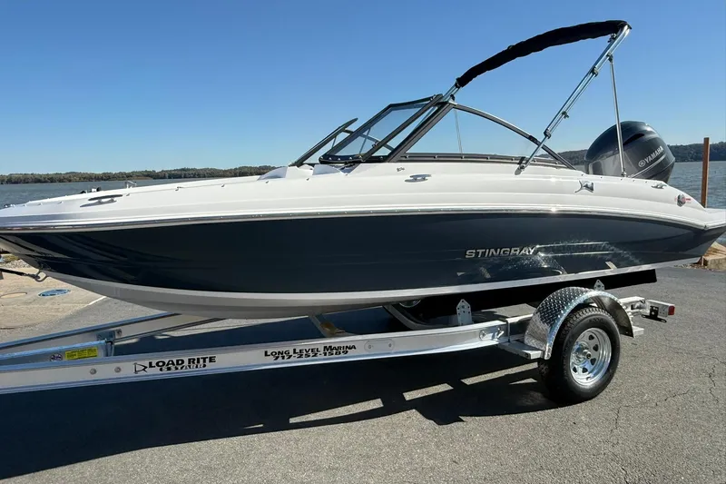 The Image of 2026 Stingray 191 DC boat on trailer by waterfront, clear sky background. - 1