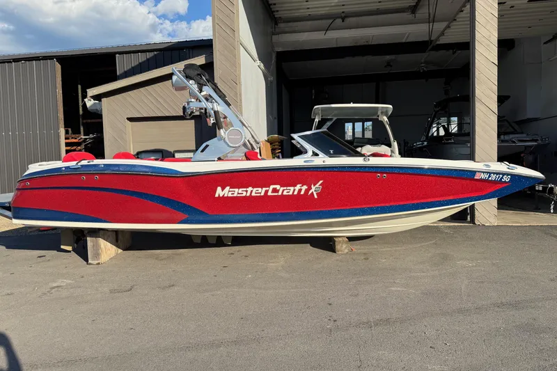 The Image of 2018 MasterCraft X46 boat in red and blue, parked outside a garage. - 0