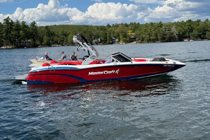 Slide: The Image of 2018 MasterCraft X46 boat on a lake with passengers, surrounded by trees and cloudy sky. - 12