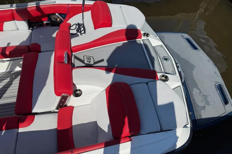 Slide: The Image of 2018 MasterCraft X46 boat interior with red and white seating, docked by water. - 2