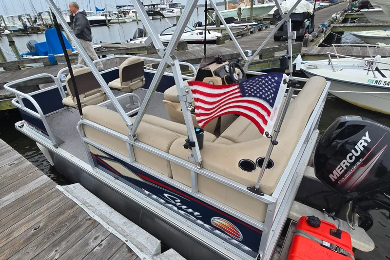 Slide: The Image of 2019 TRACKER MARINE Bass Buggy pontoon boat docked, featuring Mercury outboard motor and American flag. - 7