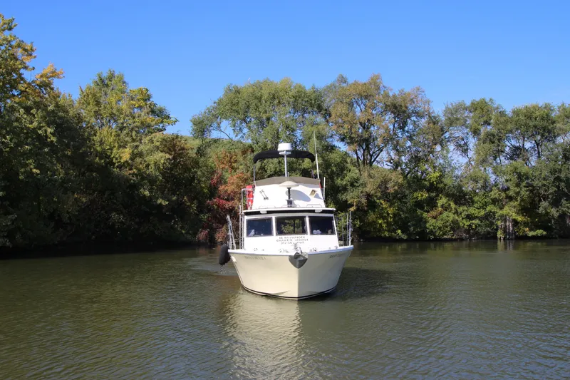Slide: The Image of 1980 Delta Boatworks 34 Offshore cruising on a serene river, surrounded by lush greenery. - 3