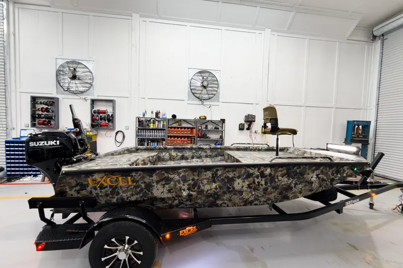 Slide: The Image of 2026 Excel Eclipse boat in workshop, camouflage design, Suzuki motor, organized tools in background. - 14