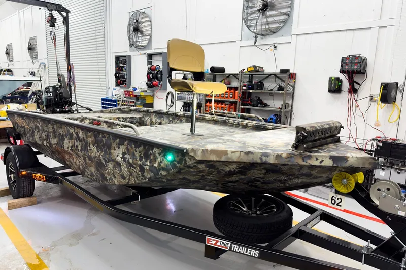 Slide: The Image of Camouflage-patterned 2026 Excel Eclipse boat on trailer in workshop setting. - 15