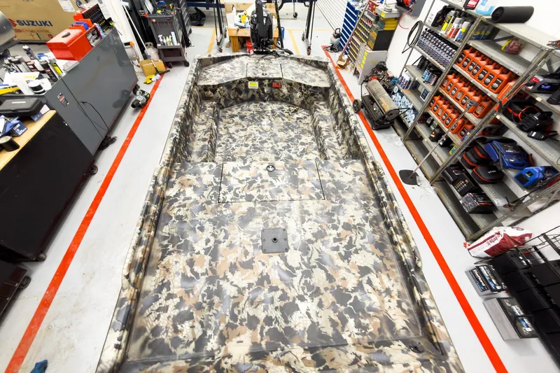 Slide: The Image of Camouflage-patterned Excel Eclipse boat in a workshop, surrounded by tools and equipment, 2026 model. - 25