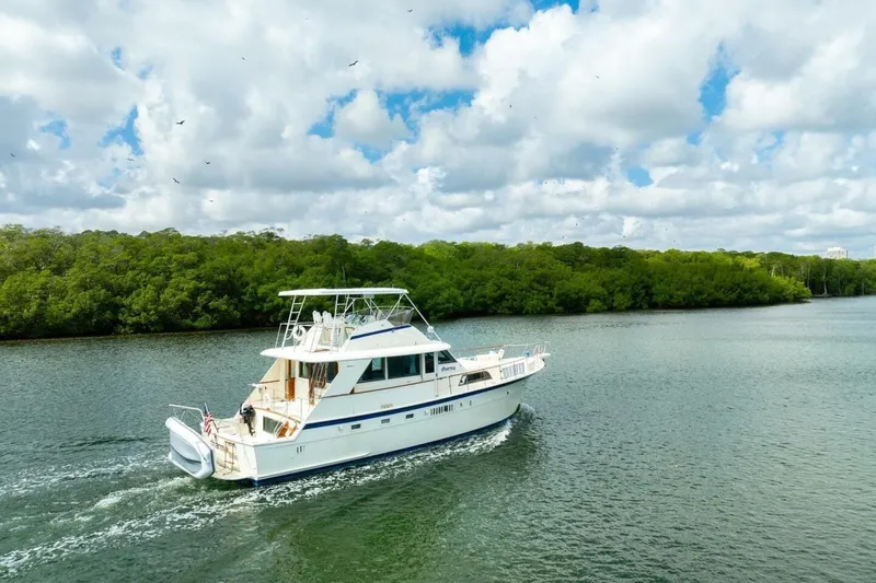 Slide: The Image of 1978 Hatteras 53 Yacht Fisherman cruising on a scenic river under a cloudy sky. - 11