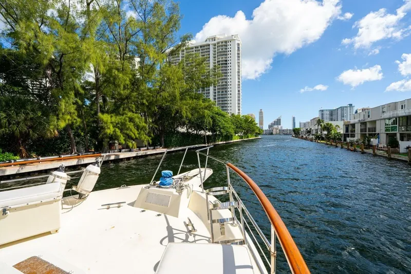 Slide: The Image of 1978 Hatteras 53 Yacht Fisherman cruising a scenic urban waterway with lush greenery. - 18