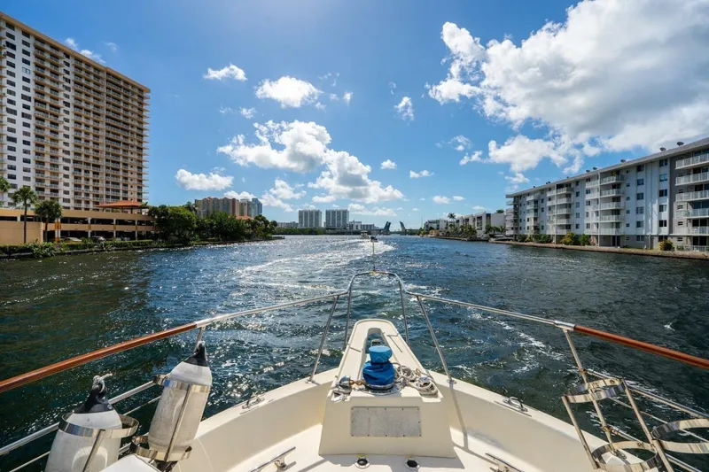 Slide: The Image of 1978 Hatteras 53 Yacht Fisherman cruising between waterfront buildings under a clear blue sky. - 19