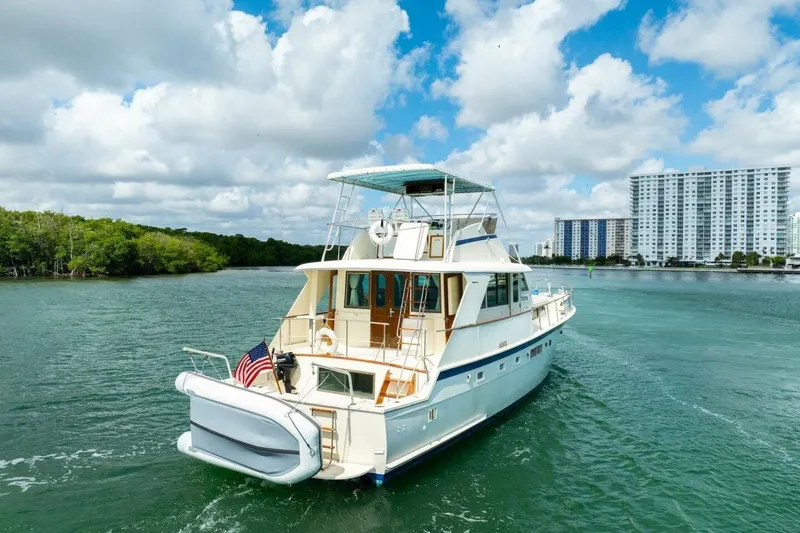 The Image of 1978 Hatteras 53 Yacht Fisherman cruising on a scenic waterway with lush greenery and buildings. - 2
