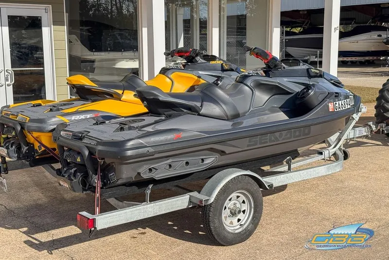 Slide: The Image of 2023 Sea-Doo RXT-X 300 jet skis on trailer, parked outside dealership. - 2