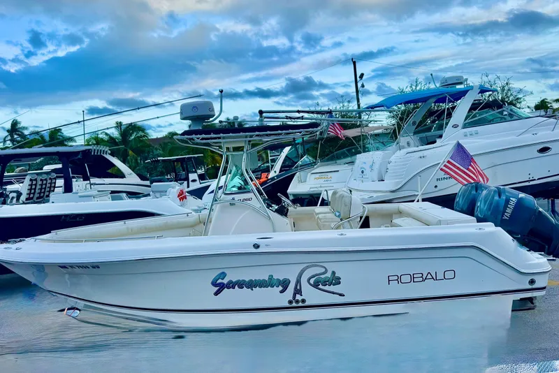 Slide: The Image of 2004 Robalo R260 Center Console boat at marina, clear sky, palm trees, parked cars. - 7