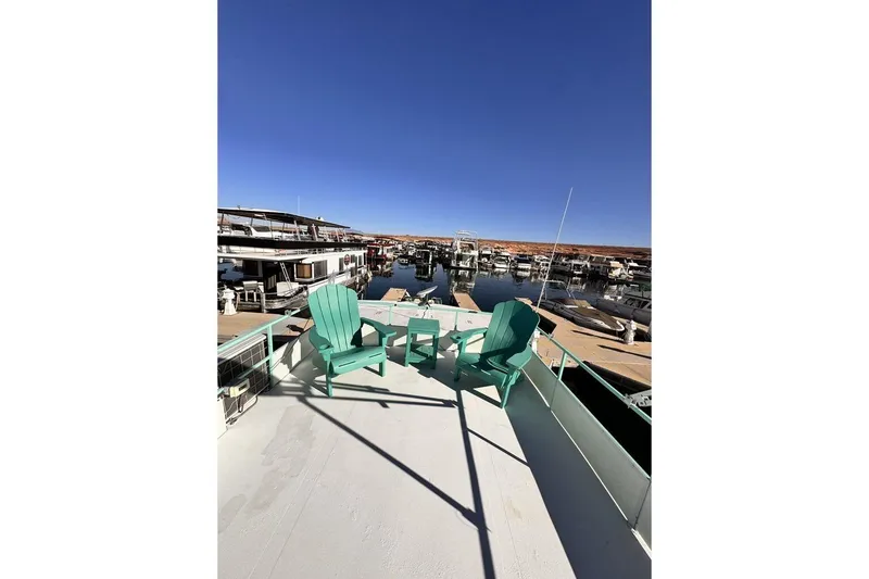Slide: The Image of 1984 Boatel Hercules houseboat deck with turquoise chairs, docked in a marina under clear blue skies. - 24