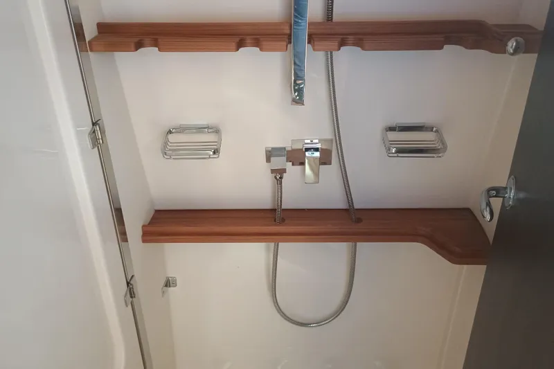 Slide: The Image of 2025 Grady-White Canyon 456 shower area with wooden shelves and chrome fixtures. - 43