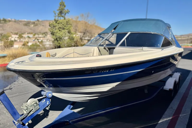 Slide: The Image of 2006 Bayliner 215 Bowrider boat on trailer, blue and white, parked outdoors. - 4