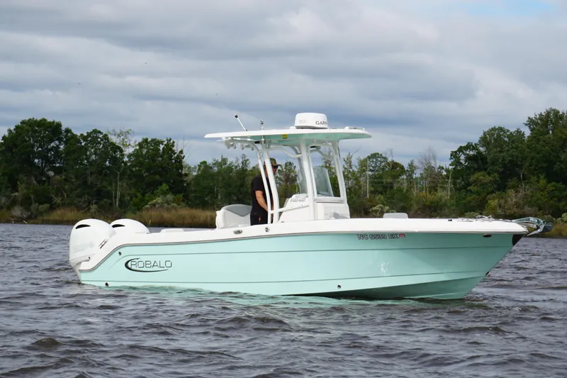 The Image of 2022 Robalo R242 Center Console boat on water, surrounded by trees and cloudy sky. - 1