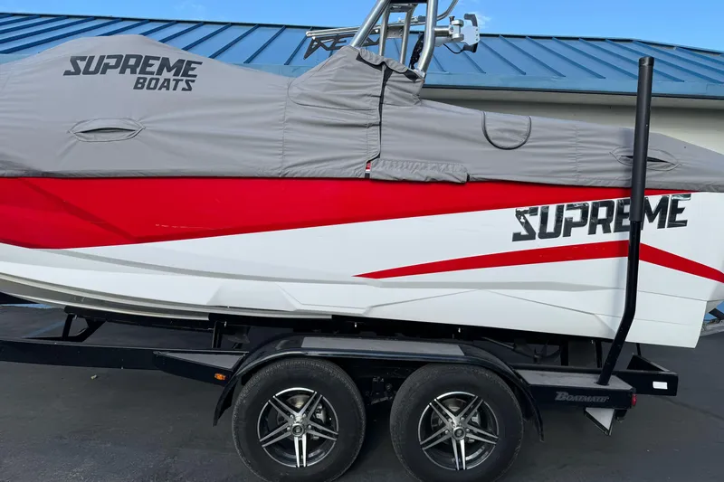 Slide: The Image of 2023 Supreme ZS212 boat with cover on trailer, under a partly cloudy sky. - 2