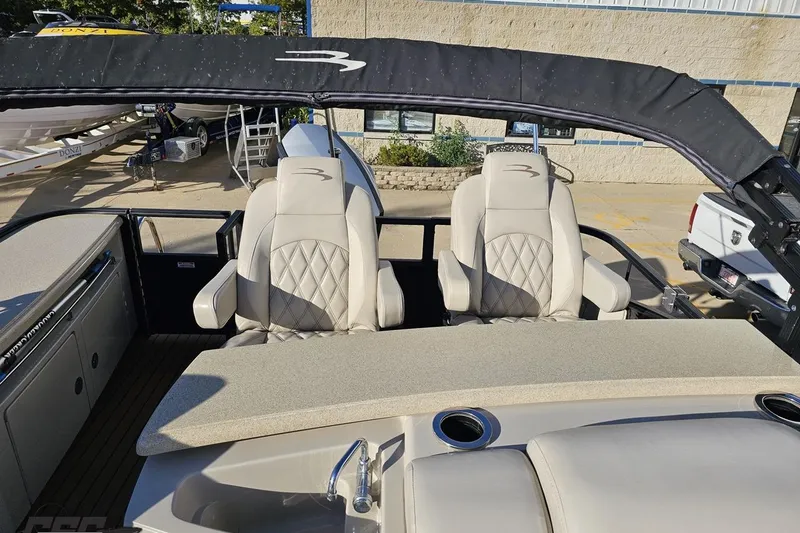Slide: The Image of 2015 Bennington 2550 QBR boat with beige seating and canopy, parked outdoors. - 92