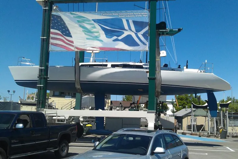 Slide: The Image of 1980 Santa Cruz SC 50 sailboat in dry dock, with vehicles and flags nearby. - 15