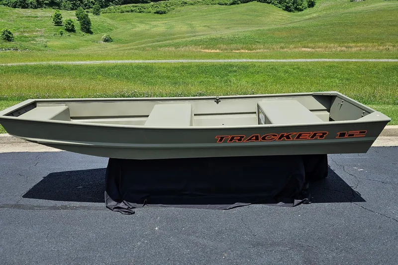 The Image of 2026 Tracker Grizzly 12 Jon boat on display, set against a lush green landscape. - 0