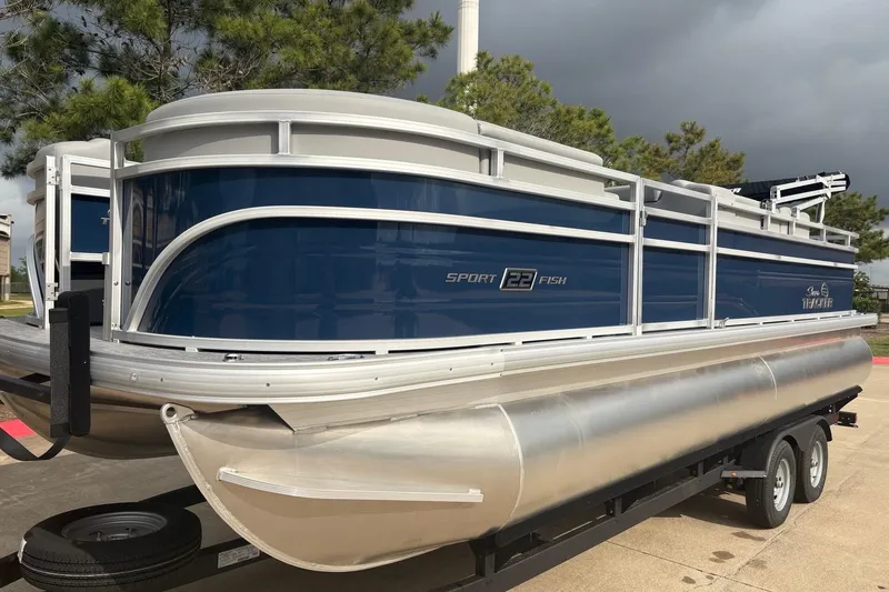 The Image of 2026 Sun Tracker SportFish 22 DLX pontoon boat on trailer, blue and silver design. - 0