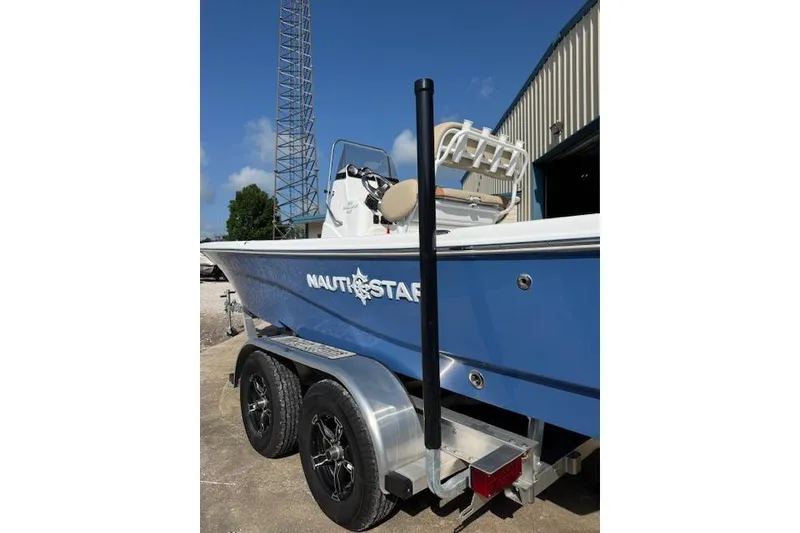 Slide: The Image of 2025 NauticStar 214 Shallow Bay boat on trailer, blue hull, outdoor setting. - 6