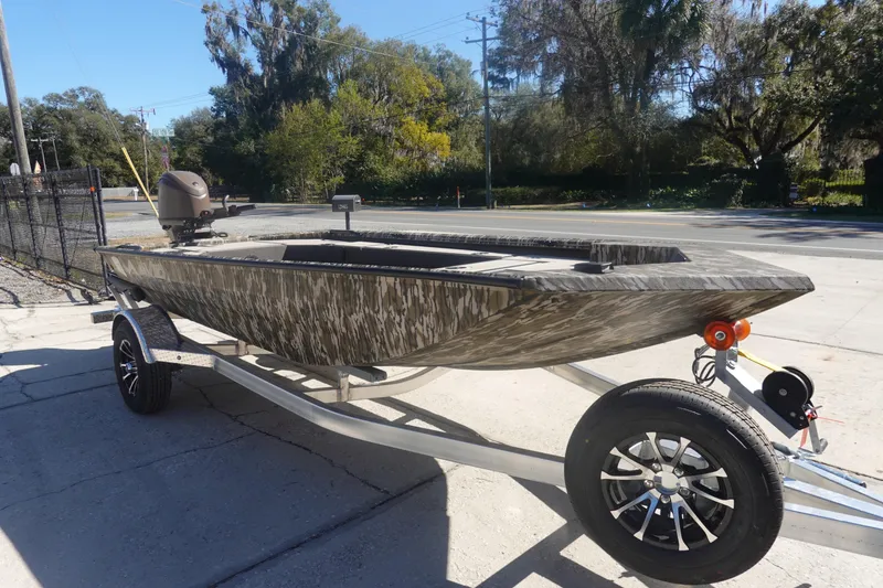 Slide: The Image of 2026 Avid 16 Commander boat on trailer, camo design, parked outdoors. - 14
