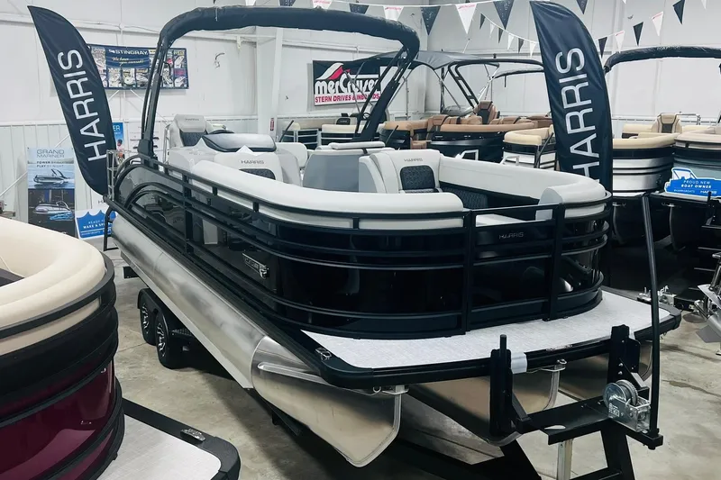 Slide: The Image of 2025 Harris Solstice 250 pontoon boat displayed in showroom with banners and seating. - 2