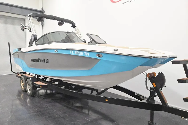 Slide: The Image of 2023 MasterCraft XT24 boat on trailer in showroom, blue and white design. - 2
