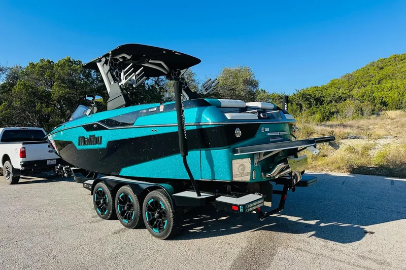 Slide: The Image of 2021 Malibu M240 boat on trailer, parked outdoors under clear blue sky. - 10