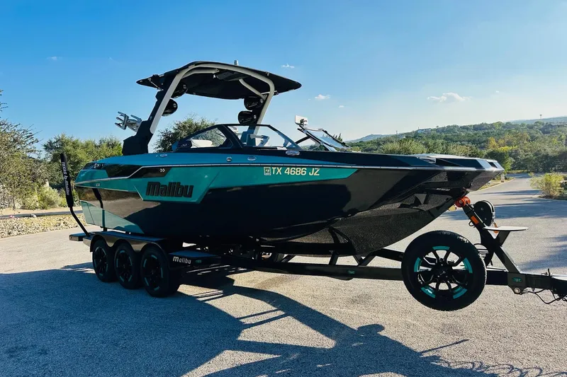 Slide: The Image of 2021 Malibu M240 boat on trailer, parked outdoors under clear blue sky. - 11