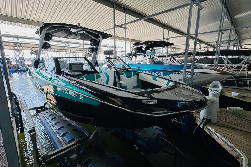 Slide: The Image of 2021 Malibu M240 boat in marina, sleek design, black and teal accents, docked under shelter. - 14