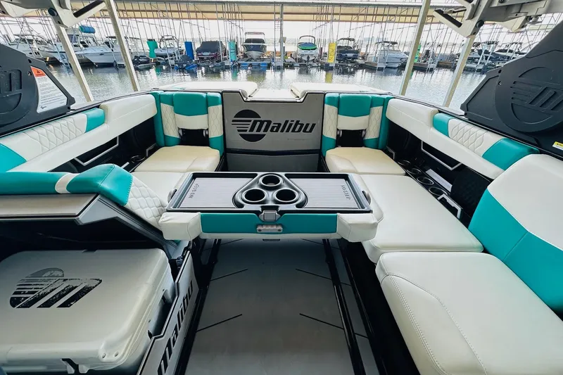 Slide: The Image of 2021 Malibu M240 boat interior with teal and white seating, cup holders, and logo. - 21