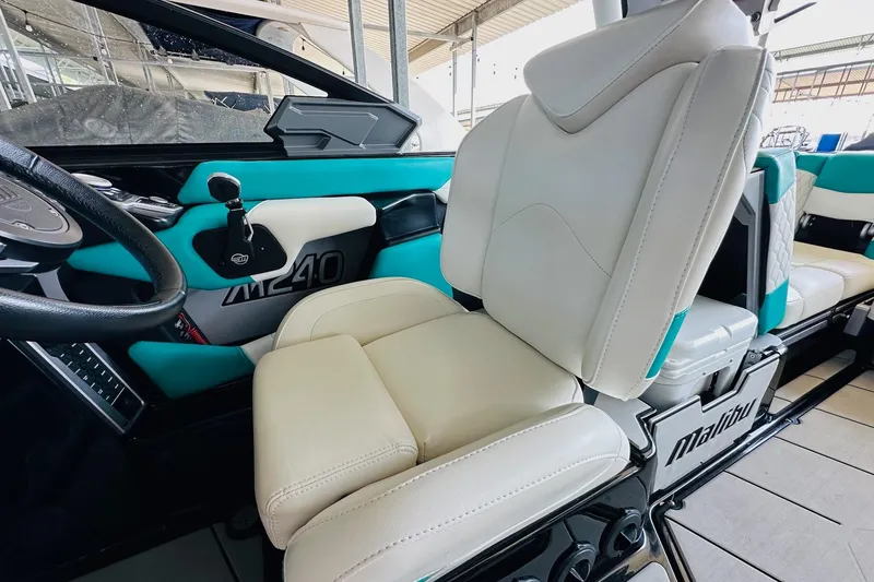 Slide: The Image of 2021 Malibu M240 boat interior with white and teal seating, steering wheel, and dashboard. - 22