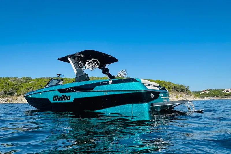 Slide: The Image of 2021 Malibu M240 boat on water, clear blue sky, scenic shoreline background. - 3