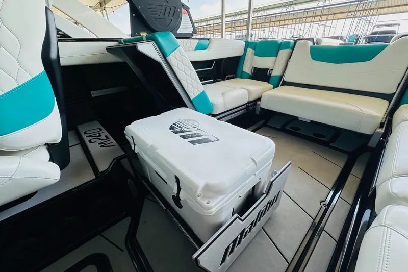 Slide: The Image of 2021 Malibu M240 boat interior with teal and white seating, featuring a central cooler. - 31