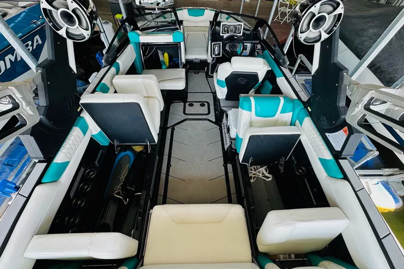 Slide: The Image of 2021 Malibu M240 boat interior with white and teal seating, advanced dashboard, and speakers. - 34