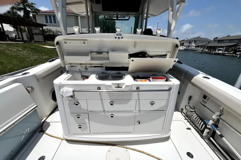 Slide: The Image of 2019 Boston Whaler 330 Outrage boat with open storage compartments and sink, docked by waterfront homes. - 6